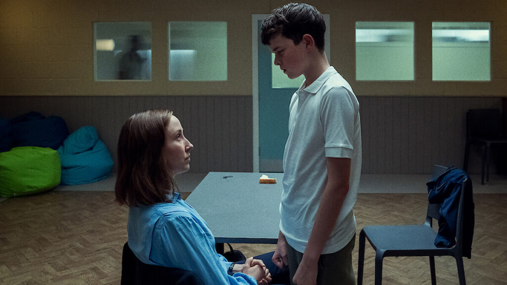 A still photo from Netflix's Adolescence showing a 13-year-old boy standing menacingly over a seated adult woman