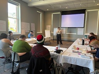 A person giving a presentation stands in front of a seated group.